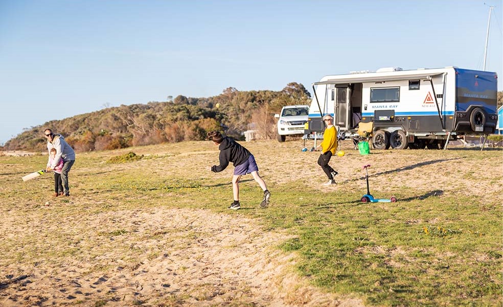 Family playing cricket in front of New Age caravan