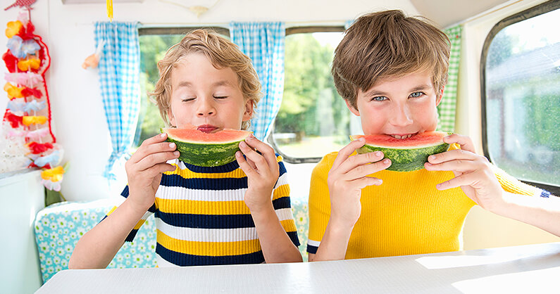 2 Boys eating watermelon inside a caravan